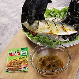Tangan membumbui ikan dengan Selera Bumbu Goreng Serbaguna dari Kobe, mangkuk bumbu dan kemasan produk terlihat