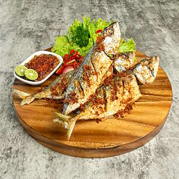Ikan goreng berbumbu Selera Bumbu Goreng Serbaguna disajikan di atas talenan kayu dengan sambal, jeruk nipis, dan sayuran segar